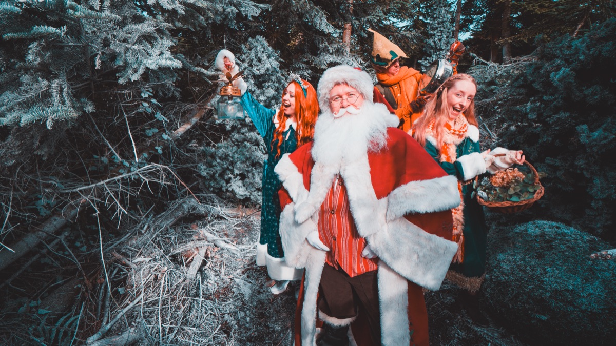 Father Christmas walking through the frosted forest with the residents of Nollaig behind him