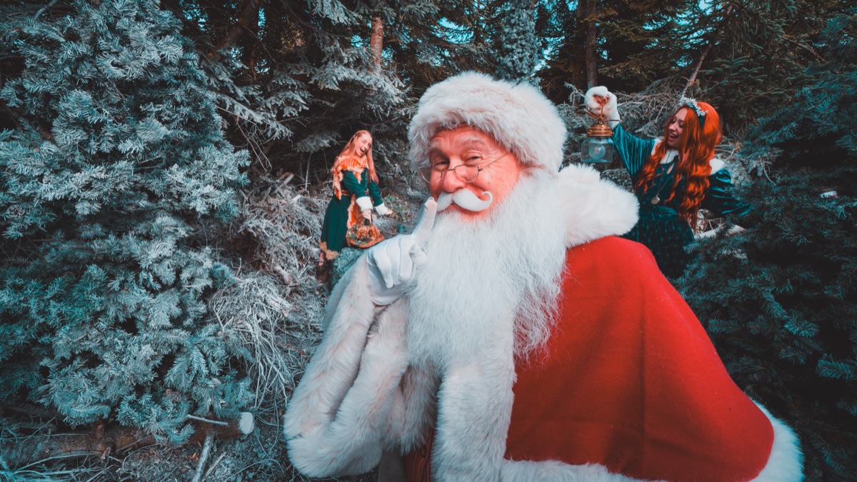 Father Christmas smiling among the trees with residents behind him